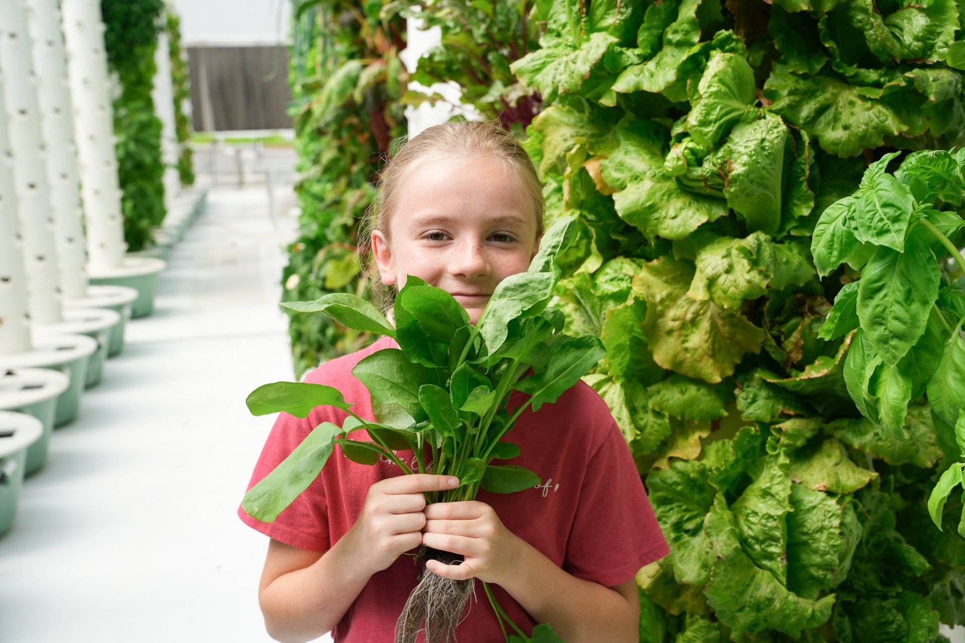 Young girl holding freshly harvested greens beside a vertical grow tower